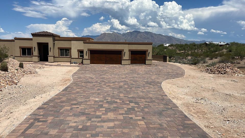 A modern single-story house in Fountain Hills with a wide, paved driveway, surrounded by desert landscaping and professional artificial grass installation, set against mountains and a partly cloudy sky.