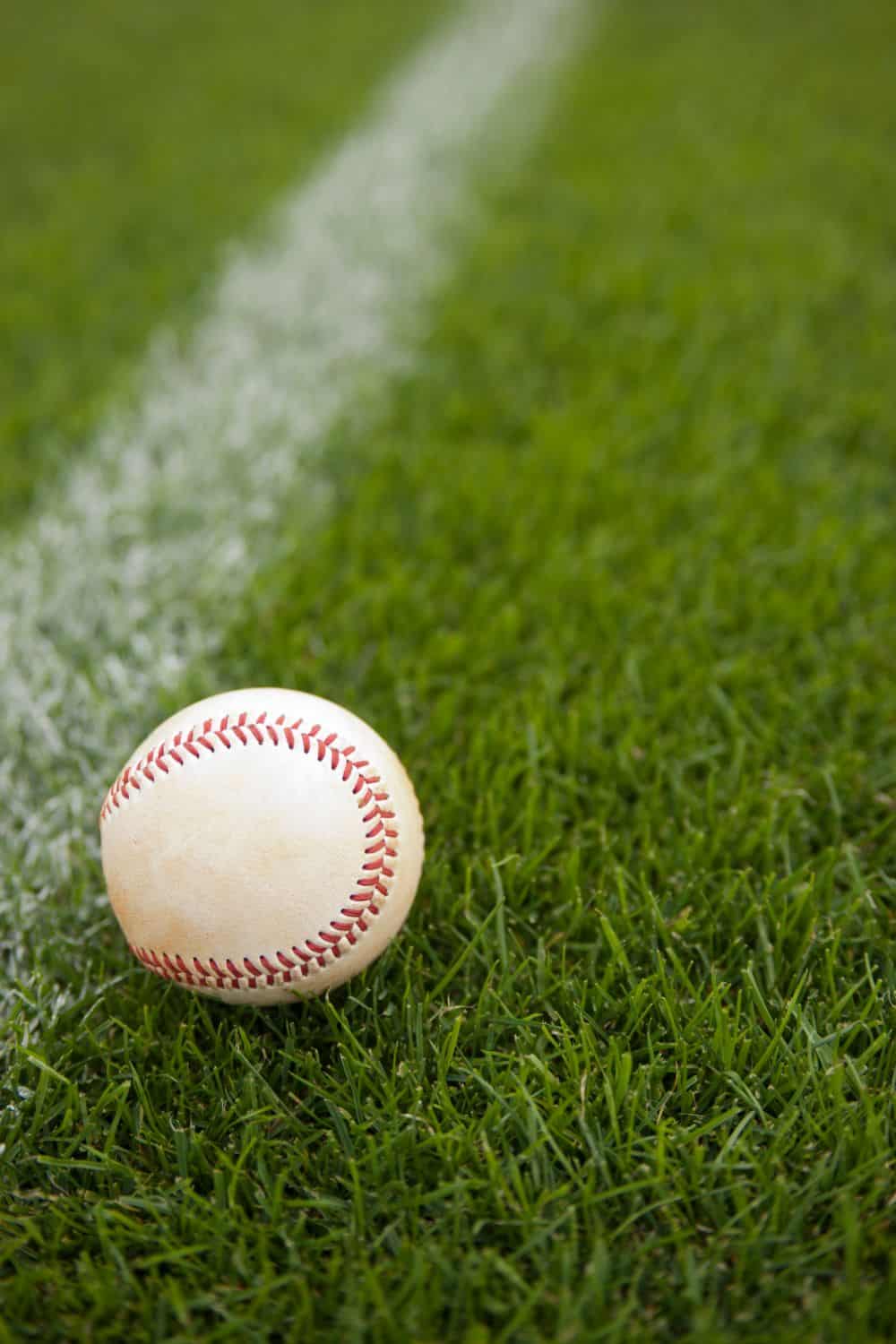 A baseball resting on bright green artificial grass near a white foul line highlights the quality of artificial turf installation in Fountain Hills.
