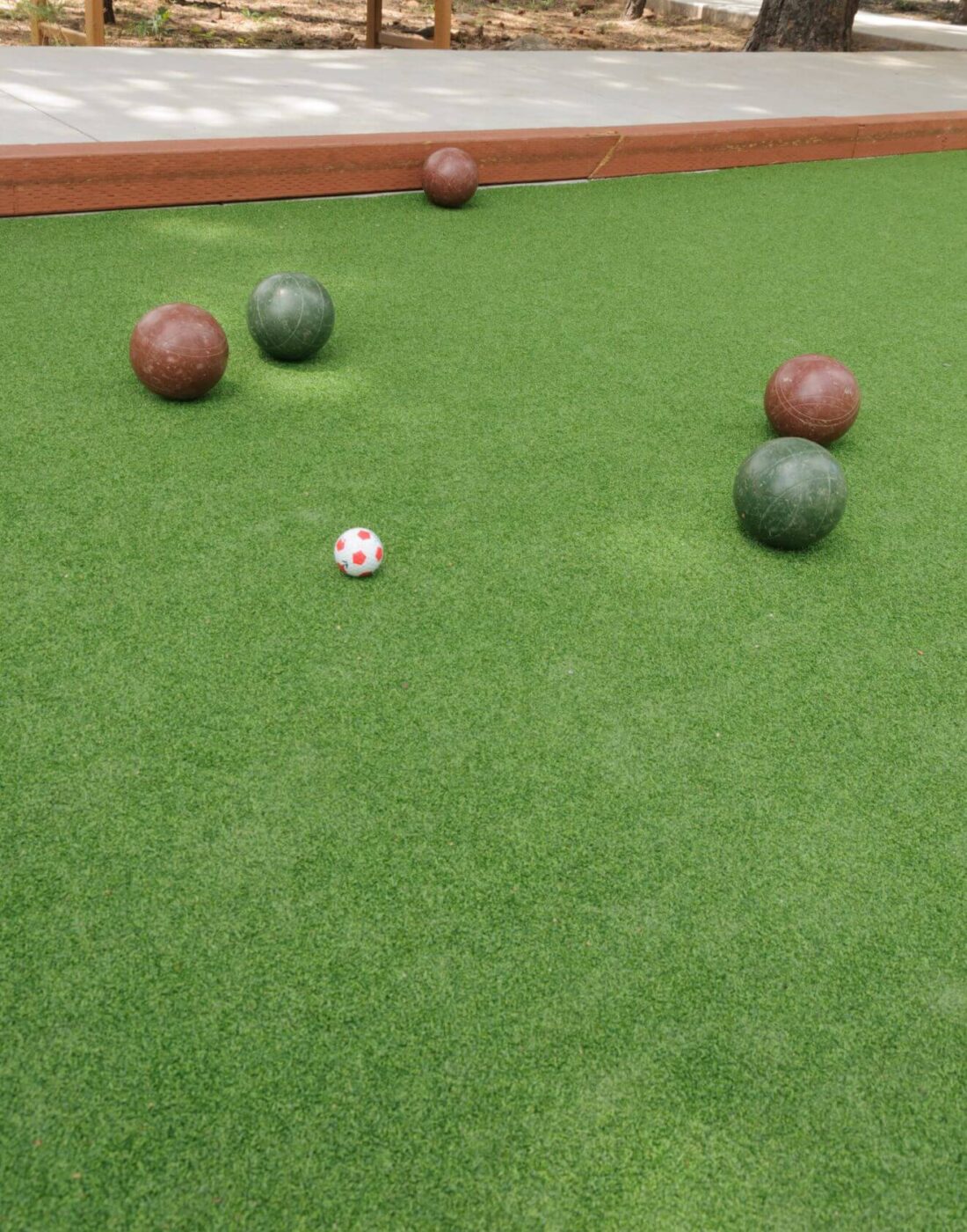 A bocce ball court in Fountain Hills features artificial turf installation, with four bocce balls—two green and two brown—arranged around a small white ball with red dots on the lush artificial grass.